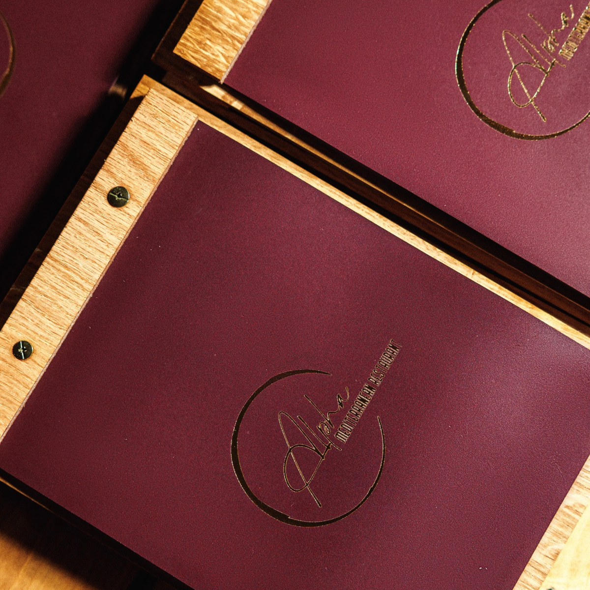 Burgundy menu covers with wood borders and gold restaurant logos